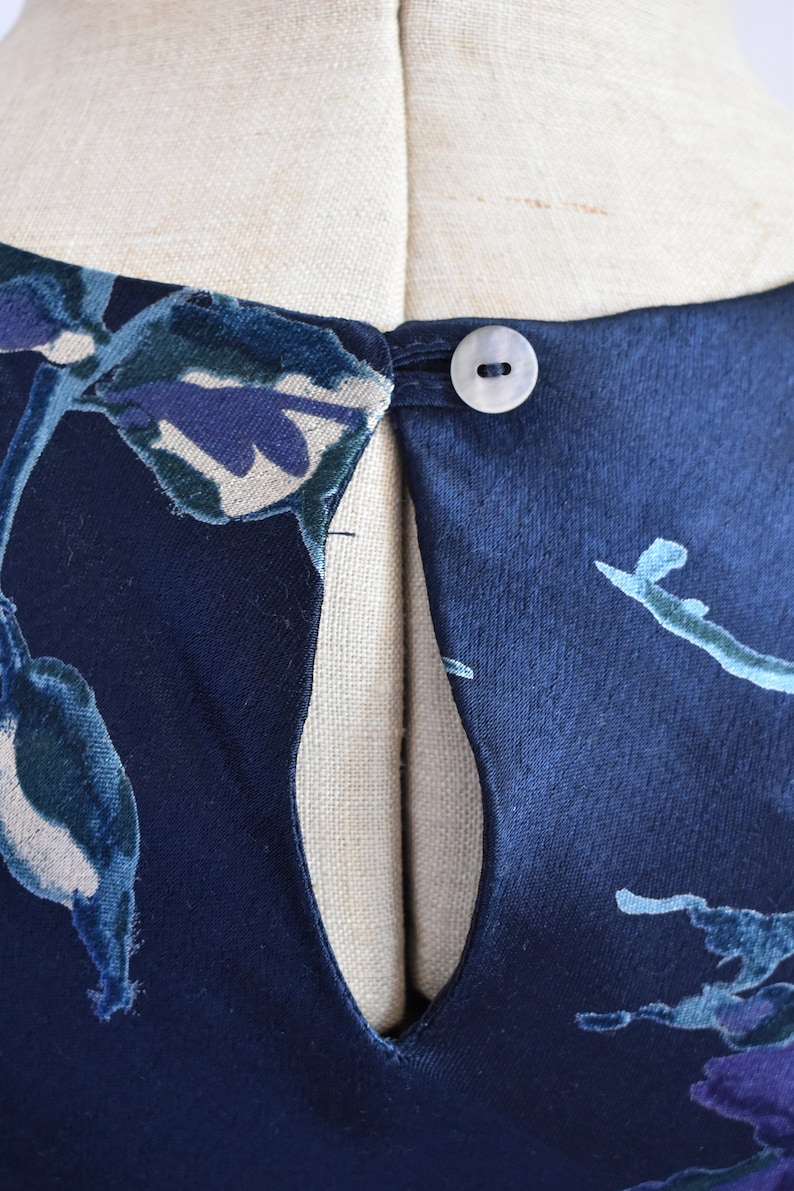 K&ouml;nnte beinhalten: Ein marineblaues Samtkleid mit Blumendruck und einem Schl&uuml;sselschl&uuml;sselloch am R&uuml;cken. Das Kleid hat einen einzigen Knopfverschluss am Nacken.