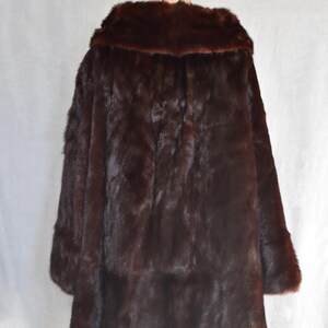 May include: A dark brown fur coat displayed on a mannequin. The coat has a wide collar and long sleeves. The fur appears dense and luxurious, with a rich, deep color. The coat is a classic outerwear garment.