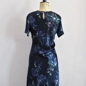 K&ouml;nnte beinhalten: Ein dunkelblaues Seidenkleid mit Blumenmuster. Das Kleid hat einen runden Ausschnitt und kurze &Auml;rmel. Das Kleid ist am Oberk&ouml;rper figurbetont und weitet sich zu einem leicht ausgestellten Rock.