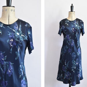 K&ouml;nnte beinhalten: Ein marineblaues Midikleid mit einem Blumendruck mit blauen, gr&uuml;nen und wei&szlig;en Blumen. Das Kleid hat kurze &Auml;rmel und einen runden Ausschnitt.