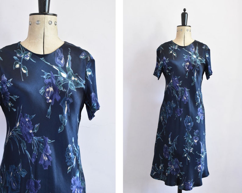 K&ouml;nnte beinhalten: Ein marineblaues Midikleid mit einem Blumendruck mit blauen, gr&uuml;nen und wei&szlig;en Blumen. Das Kleid hat kurze &Auml;rmel und einen runden Ausschnitt.