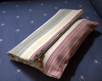 May include: A striped fabric clutch purse with a zipper closure and a wooden zipper pull. The purse is pink, beige, and green.