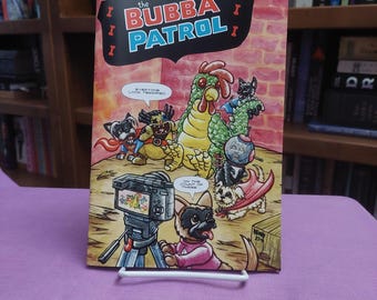 May include: A comic book titled The Bubba Patrol issue number 5, featuring a colorful illustration of a large green chicken and several small dogs in capes. One dog operates a video camera on a tripod, while speech bubbles contain text.
