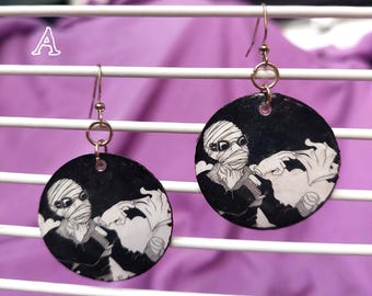May include: A pair of round dangle earrings featuring a black and white illustration of a bandaged figure wearing goggles and a dark coat. The circular charms hang from silver-toned metal hooks. The letter A is visible in the upper left corner.