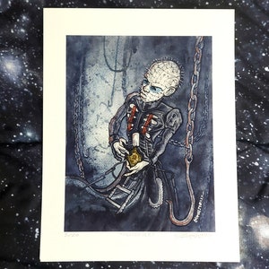 Puede incluir: Una ilustración de acuarela de un personaje de la película de terror "Hellraiser" sosteniendo una caja con forma de corazón. El personaje se representa con una tez pálida, la cabeza rapada y una boca grande abierta. El personaje lleva un atuendo de cuero negro con una cadena unida a un gancho. El fondo es un escenario oscuro y sombrío.