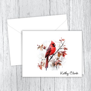May include: A red cardinal bird perched on a branch with red berries and brown leaves. The bird is painted in a watercolor style. The image has the name "Kathy Clark" written at the bottom.