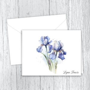 May include: A watercolor painting of two blue irises with a white background. The artist's name, Lynn Travis, is written in cursive at the bottom of the card.