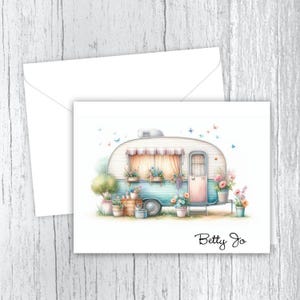 Puede incluir: Una caravana vintage blanca y azul con una puerta rosa, rodeada de flores y plantas. El texto "Betty Jo" está escrito debajo de la caravana.
