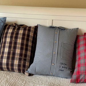 May include: Four decorative pillows made from repurposed shirts with embroidered messages. The pillows are in various plaid patterns, including blue, brown, gray, and red.
