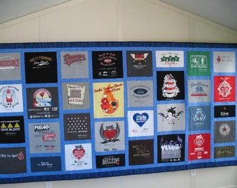 May include: A blue quilt made from t-shirts with various designs and slogans related to blood donation. The quilt is made up of 36 squares, each with a different design. Some of the designs include a red heart, a blood drop, and the words "Give Blood".