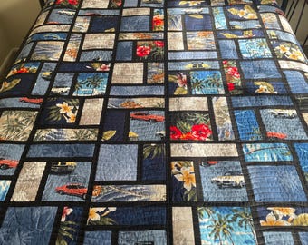 May include: A black and blue patchwork quilt with a Hawaiian theme. The quilt features palm trees, flowers, and cars. The quilt is made of different fabrics and is quilted with a black thread.