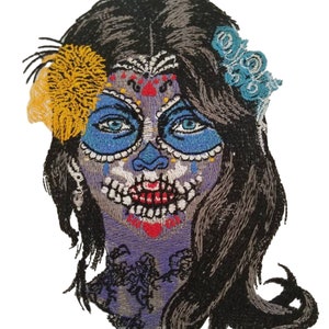 May include: Embroidered patch featuring a stylized sugar skull design. The skull has blue eye sockets and a blue nose, with intricate patterns in red, white, and gray. The hair is black, and the design includes yellow and blue floral accents.