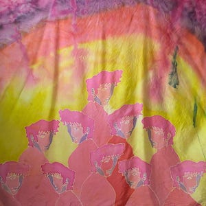 Könnte beinhalten: Ein Seidentuch mit einem Batik-Muster in Rosa-, Gelb- und Lilatönen. Das Tuch zeigt ein sich wiederholendes Muster aus stilisierten Gesichtern in Rosa.