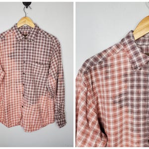 May include: A long-sleeved plaid shirt with a brown and pink color scheme. The shirt has a faded, ombre effect, with the brown color fading into the pink color.