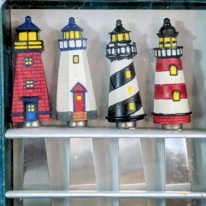 May include: A set of four Boston Warehouse spreaders with lighthouse-shaped handles. The handles feature distinct designs: a red brick lighthouse, a white lighthouse with a red door, a black and white spiral lighthouse, and a red and white striped lighthouse.