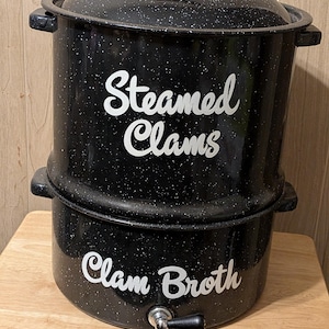 May include: Black speckled enamel pot with lid and handle, labeled "Steamed Clams" and "Clam Broth" in white script. Features a spigot near the base. A kitchenware item for preparing seafood.