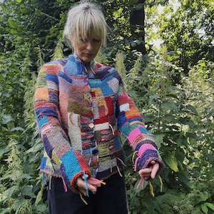 Puede incluir: Chaqueta de punto de estilo patchwork colorido con cierre de botones. La chaqueta presenta una variedad de colores, incluyendo azul, rojo, amarillo y verde. Las mangas son largas y la chaqueta parece hecha a mano.