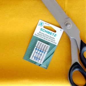 May include: A package of 5 Schmetz Microtex (Sharp) sewing needles, size 90/14, on a yellow fabric with a pair of silver scissors.