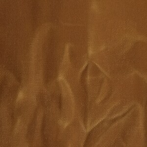 A close-up of a brown fabric with a textured surface. The fabric is wrinkled and has a light brown sheen.