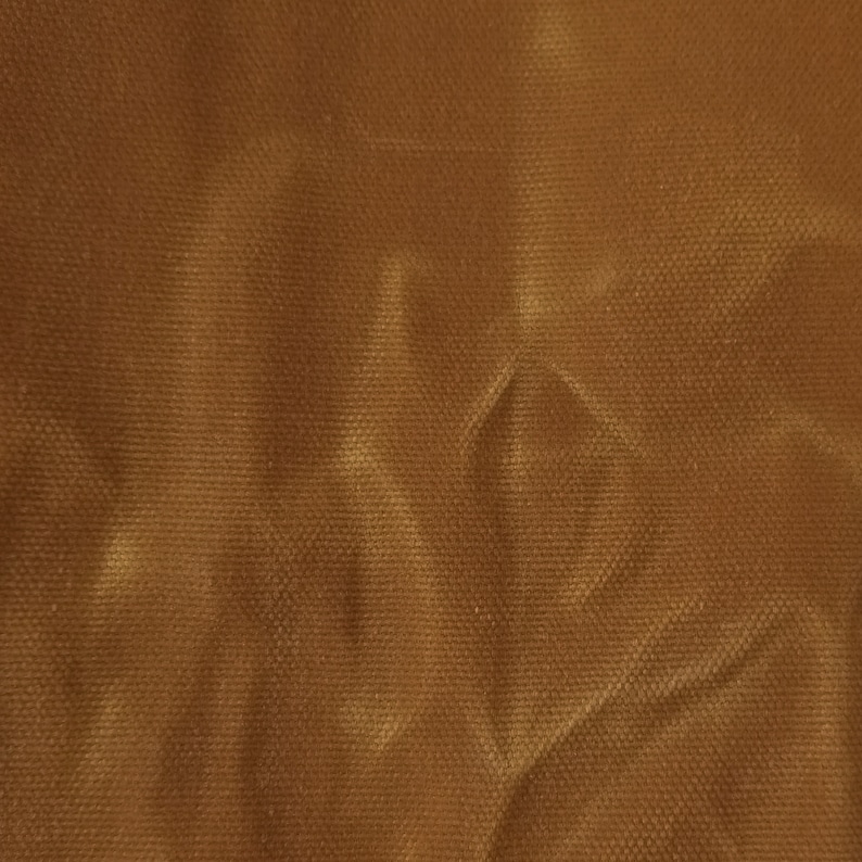 A close-up of a brown fabric with a textured surface. The fabric is wrinkled and has a light brown sheen.