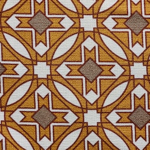 Puede incluir: Primer plano de una tela con un patrón geométrico repetitivo. El diseño presenta una combinación de formas amarillo mostaza, blancas y marrones. El patrón incluye elementos de diamante y cruz, creando un diseño simétrico y visualmente atractivo.
