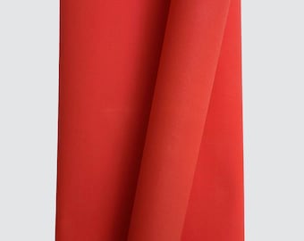Puede incluir: Un rollo de tela roja brillante. La tela es lisa y tiene un ligero brillo.