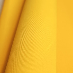 Close-up of yellow waxed cotton twill fabric with a textured surface.