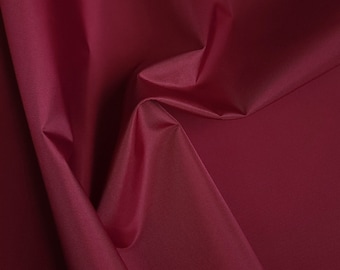 May include: Close-up of a deep red fabric with a smooth, silky texture. The fabric is folded and draped, creating soft folds and wrinkles.