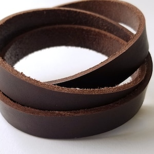 May include: A close-up of a brown leather cord, rolled up in a circle. The cord is smooth and has a slightly textured surface.