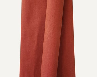 Peut inclure: Gros plan sur un tissu plié de couleur rouille. Le tissu a une surface légèrement texturée et est drapé en plis souples, créant des ombres et de la profondeur. La couleur est une teinte chaude et terreuse.