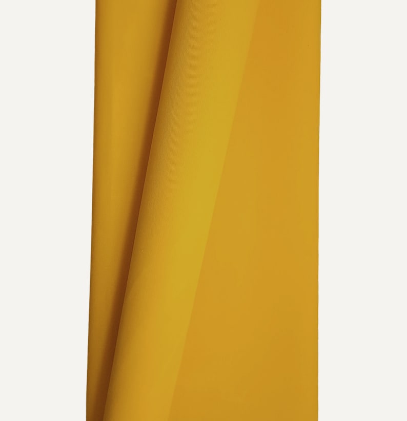 A close-up of a yellow waxed cotton twill fabric folded in half. The fabric is smooth and has a subtle sheen.