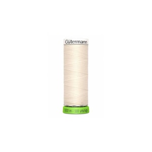 May include: A spool of off-white Gütermann thread. The cylindrical spool has a green base and a white label with "100 m - 110 yds/vgs". The Gütermann logo is printed on the top. The thread is wound neatly.