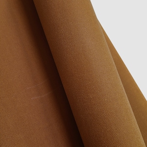 Close-up of a brown fabric with a textured surface. The fabric is folded over itself, creating a diagonal line.