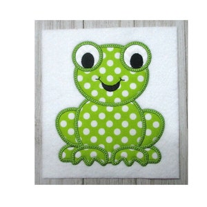 May include: Green felt applique of a frog with white polka dots. The frog has large black eyes and a stitched-on smile.