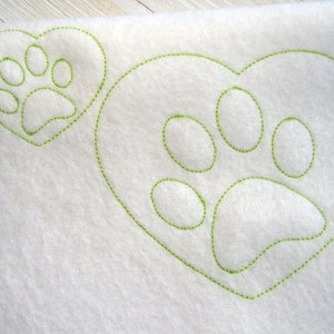 May include: White fabric with two green stitched paw prints in the shape of hearts.