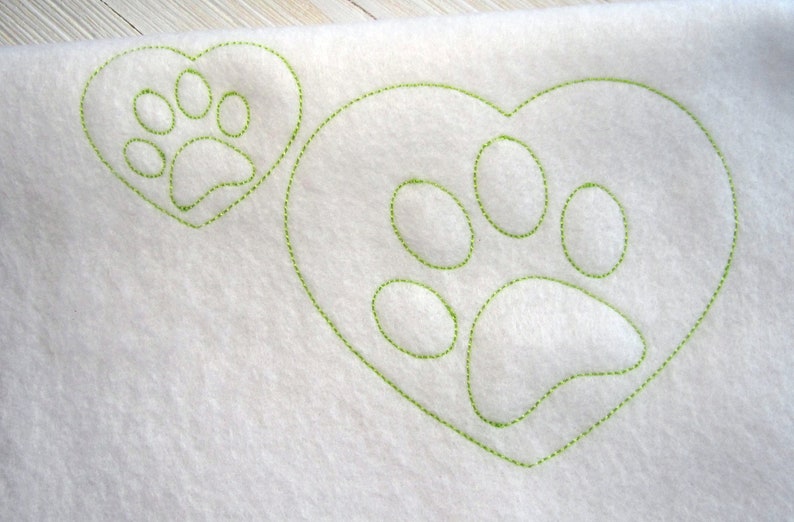 May include: White fabric with two green stitched paw prints in the shape of hearts.