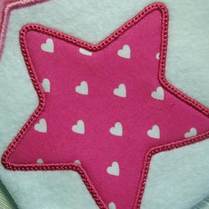 May include: A pink star-shaped patch with white hearts on a white fabric background.
