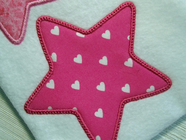 May include: A pink star-shaped patch with white hearts on a white fabric background.
