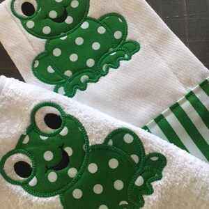 May include: Two white towels with green and white polka dot frogs embroidered on them. The towels have a green and white striped border.