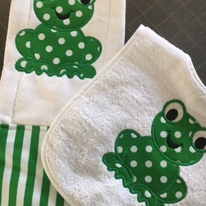 May include: A set of two white towels with green frog appliques. The towels have a white background with green polka dots. The towels are made of soft, absorbent material.