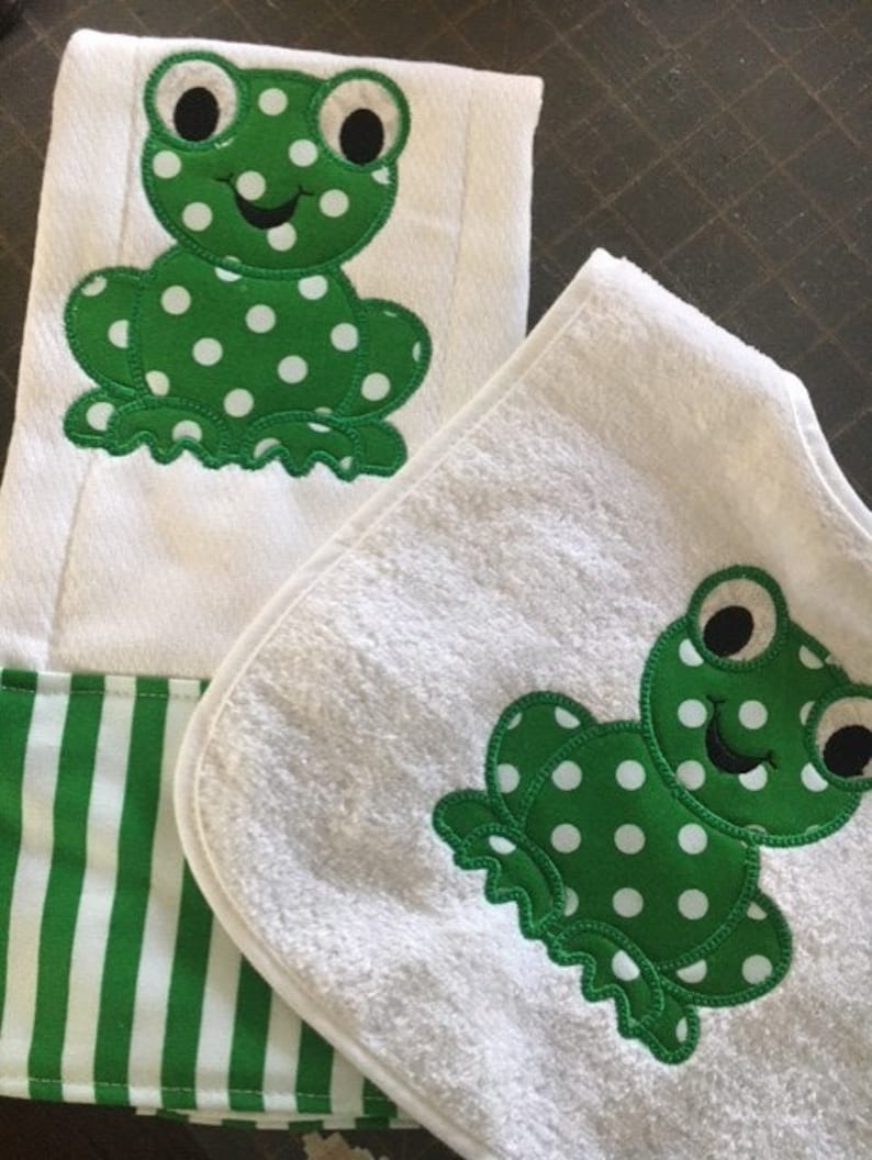 May include: A set of two white towels with green frog appliques. The towels have a white background with green polka dots. The towels are made of soft, absorbent material.