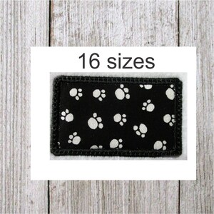 May include: Black fabric patch with white paw prints, surrounded by a black stitched border. The text "16 sizes" is printed above the patch.