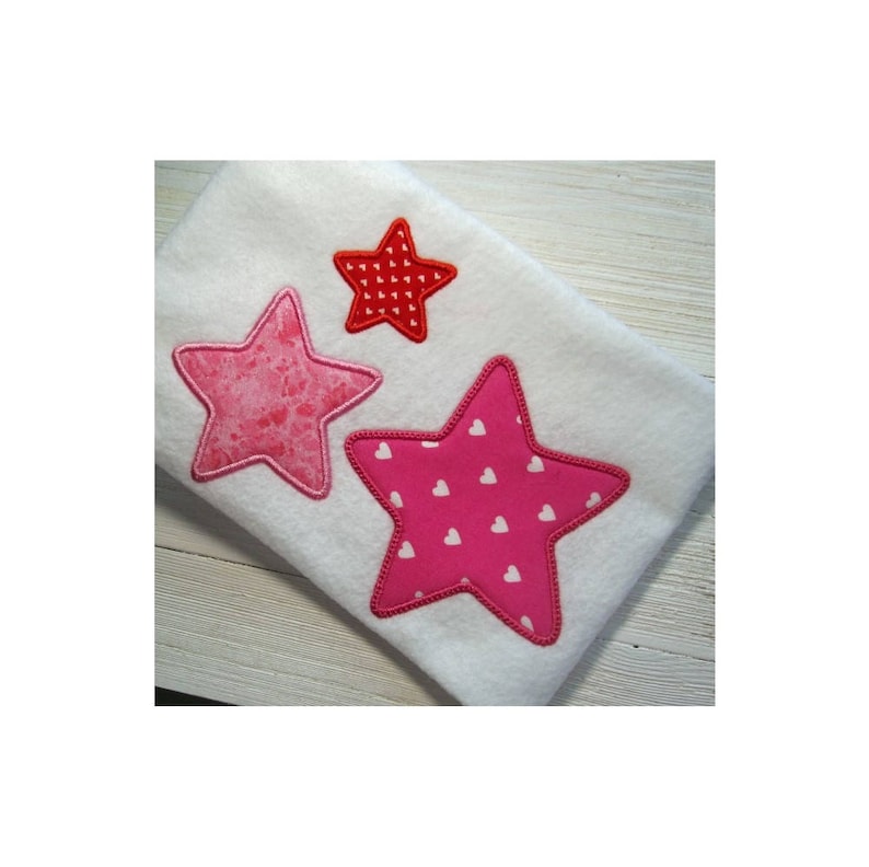 May include: Three embroidered stars on a white fabric background. The largest star is pink with white polka dots, the middle star is pink with a marbled pattern, and the smallest star is red with a white polka dot pattern.