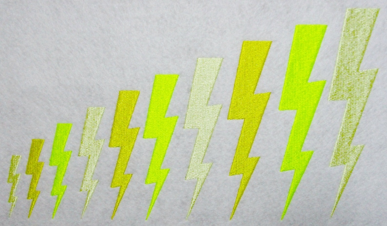 May include: A series of embroidered lightning bolts in varying shades of yellow and chartreuse are arranged diagonally on a light gray background. The bolts increase in size from left to right, creating a visual gradient.