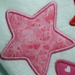 May include: A pink star with a glittery finish and a pink stitched border. The star is on a white background.