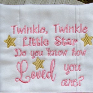 May include: A white burp cloth with pink embroidery that reads "Twinkle, Twinkle Little Star Do you know how Loved you are?" with two gold stars.