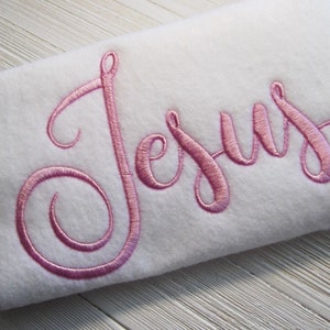 May include: White fabric with the word "Jesus" embroidered in pink cursive script.