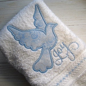 May include: White bath towel with a blue embroidered dove and the word "Joy" in cursive script.
