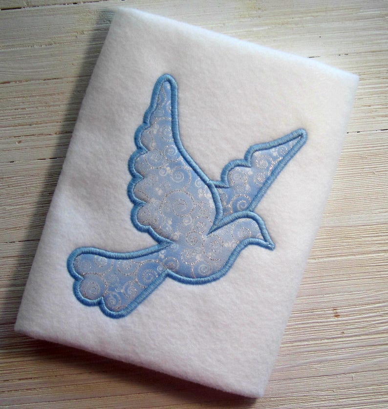 May include: A white fabric with a blue embroidered dove with a silver and blue patterned design.