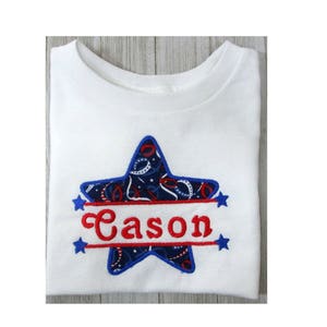 Può includere: Maglietta bianca con un design a stella blu e rossa e il nome "Cason" ricamato in rosso su uno stendardo.